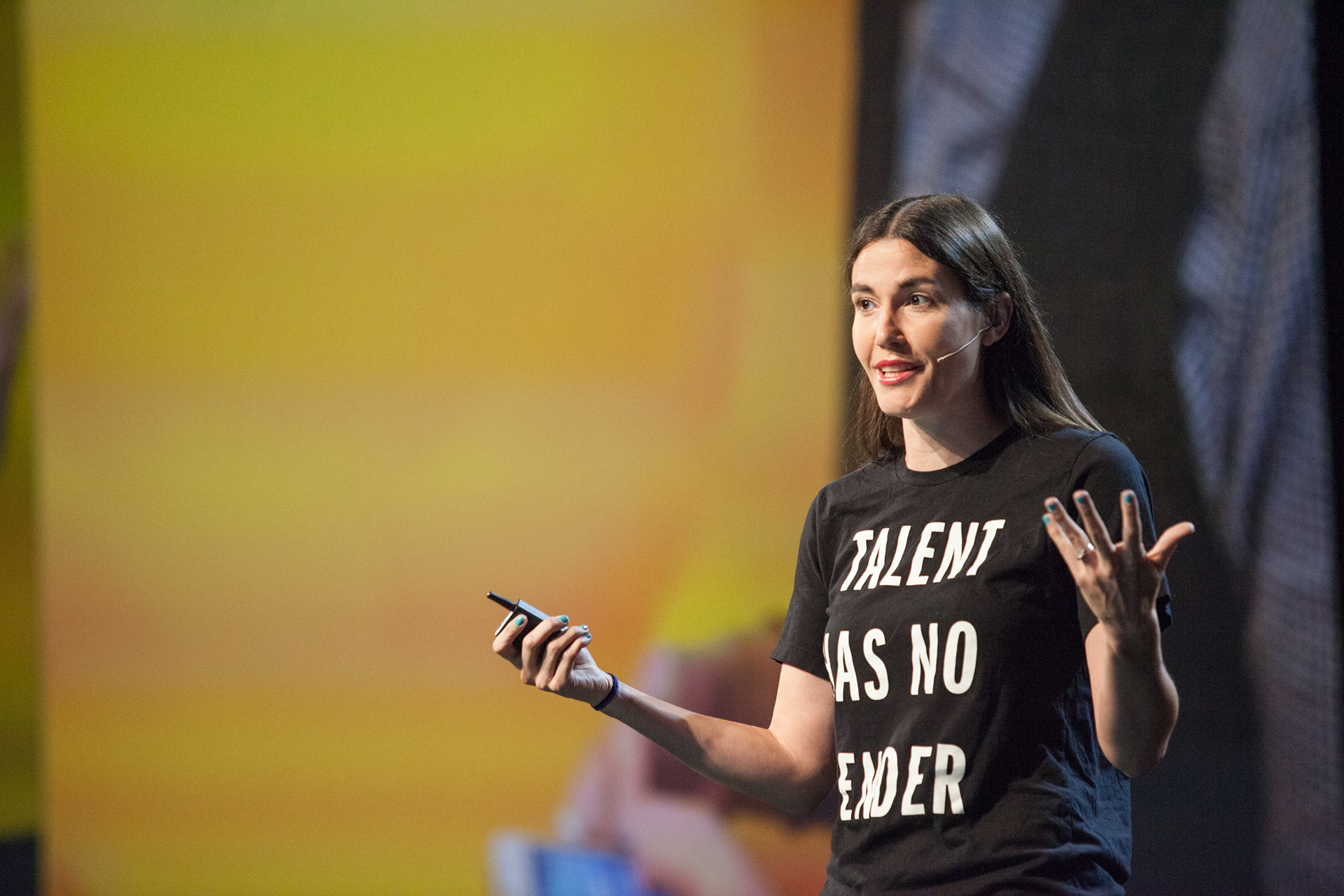 Female speaker presenting on stage wearing a Talent Has No Gender t-shirt